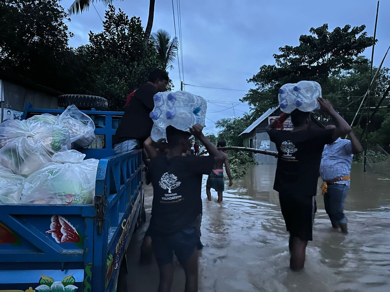 Volunteers carrying bottled water from a vehicle through floodwater